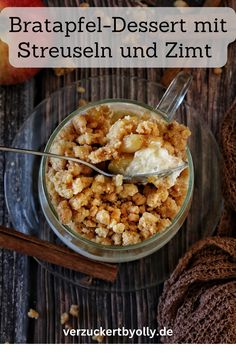 a dessert in a glass bowl on top of a wooden table next to an apple