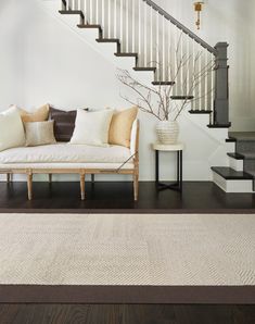 a white couch sitting under a stair case next to a table with a vase on it