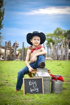 a young boy wearing a cowboy hat and sitting on top of a barrel with a sign