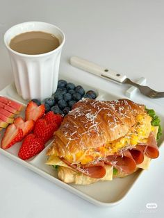 a sandwich and fruit on a plate with a cup of coffee next to it,