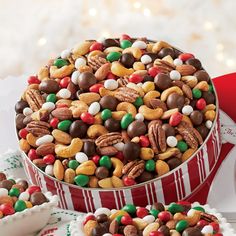 a red and white container filled with lots of candy covered food next to cookies on top of a table