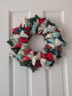 a christmas wreath hanging on the front door with red, white and green fabric bows