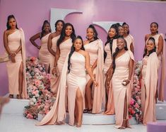 a group of women standing next to each other in front of a purple wall with flowers