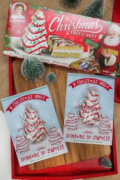 christmas tree cakes are on display in a red tray next to other holiday cards and decorations