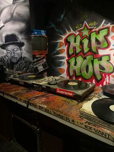 a dj booth with various records and graffiti on the wall behind it, including an old record player