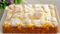 a square cake with powdered sugar on top sits on a plate next to flowers