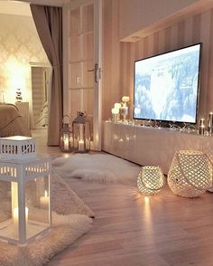 a living room filled with lots of white furniture and candles in front of a flat screen tv