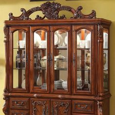 a wooden china cabinet with glass doors and ornate carvings on the top, along with other furniture