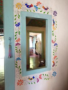 a dog is sitting in front of a mirror with flowers painted on the wall behind it