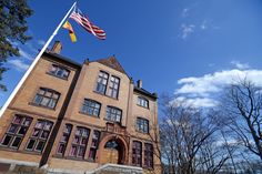 an american flag flying in front of a large brick building with trees and blue sky