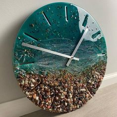 a clock that is on the wall with sand and sea shells in front of it