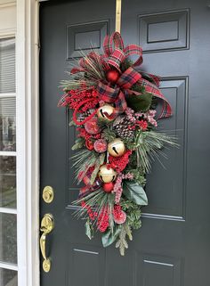 a christmas wreath on the front door with bells and pine cones hanging from it's side