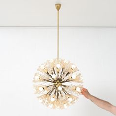 a chandelier hanging from the ceiling with two hands reaching for it to light up