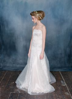 a woman in a white wedding dress standing on a wooden floor with a blue wall behind her