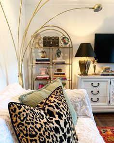 a leopard print pillow on a white bed with a gold headboard and black lamps