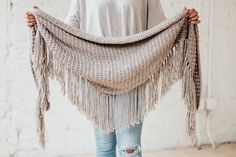 a woman holding up a crocheted shawl