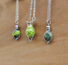 three necklaces with different designs on them sitting on a wooden surface, one is green and the other is silver