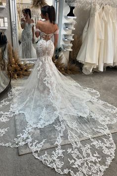 a woman standing in front of a mirror wearing a wedding dress with an open back