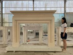 a woman standing in front of a white fireplace with columns on either side and another man looking at the fire place