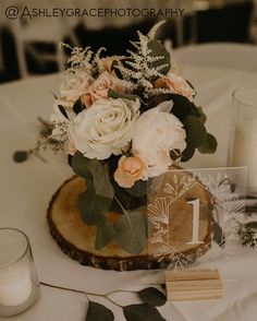 a centerpiece with flowers and greenery sits on a table next to two candles