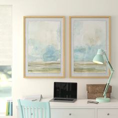 two paintings hang on the wall above a desk with a laptop computer and blue chair