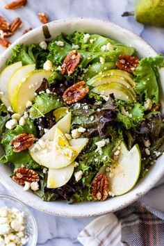 a white bowl filled with green salad and sliced apples on top of a marble table