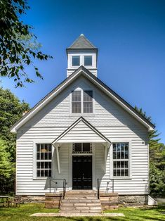 an old white church with stairs leading up to the front door and steeple on a sunny day