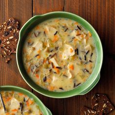 two bowls filled with soup next to crackers on top of a wooden table,