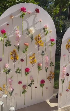 several flowers are arranged on the side of a white arch with candles and vases