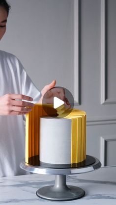 a woman is decorating a cake with gold and white icing on a marble table