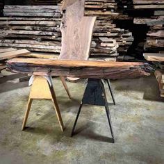 a table made out of wood and metal legs with a chair next to it in front of stacks of wooden planks