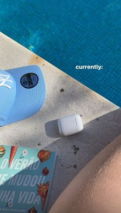 a blue hat sitting next to a book on top of a cement floor near a swimming pool