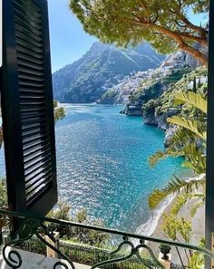 an open window looking out at the ocean and mountains from a balcony with shutters