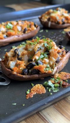 baked sweet potatoes with black olives and cheese on a baking sheet, ready to be eaten