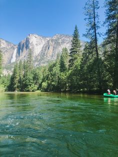 two people in a green canoe paddling down a river with mountains in the background