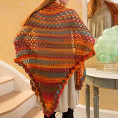 a woman standing in front of a mirror wearing a multicolored crocheted shawl