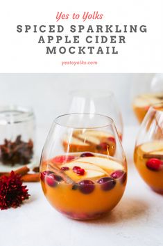 two glasses filled with liquid sitting on top of a white table next to flowers and spices