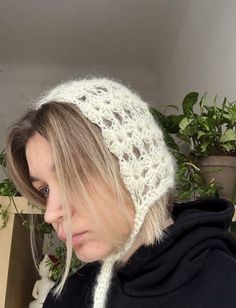 a woman wearing a white crochet headband in front of a potted plant