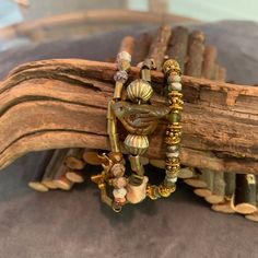 This designer bracelet beautifully depicts the 1848 gold rush along the  "Sierra River". The main strand is the river rubble showing off highly prized peach moonstone nuggets with brass tubes leading to the Czech glass bird with bronze wash. Adding in brass nuggets along the way. The panned out batea or sediment pieces make up the other two strands. Jade multi-faceted stones and brass tubes are featured in the second strand and green faceted Czech glass pieces with gold spacers complete strand 3 Artisan Gold Beaded Bracelets, Unique Multi-strand Gold Jewelry, Earthy Gold Beaded Bracelets For Healing, Adjustable Earthy Gold Jewelry, Gold Wrap Bracelet With Natural Stone Round Beads, Earthy Hand Wrapped Bracelet Jewelry, Earthy Gold Jewelry With Natural Stones, Unique Bronze Beaded Bracelet As Gift, Hand Wrapped Earthy Bracelet Jewelry