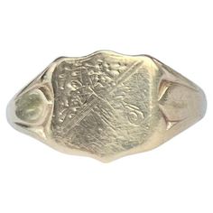 The main detail on this ring is the shield with corner engraving. The chunky shoulders are smooth and carry on down into a plain band modelled in 9ct gold. Made in Birmingham 1964, England. RIng Size: S or 9 Widest Part: 12mm Weight: 3.4g Classic Yellow Gold Engraved Ring With Coat Of Arms, Classic Oval Signet Ring With Coat Of Arms, Classic Oval Stamped Signet Ring, Classic 14k Gold Stamped Signet Ring, Classic 14k Stamped Signet Ring For Commemoration, Classic Hallmarked Signet Ring For Commemoration, Classic Signet Ring With Coat Of Arms For Anniversary, Classic Engraved Signet Ring For Commemoration, Antique 14k Stamped Signet Ring For Commemoration