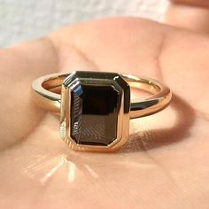 a close up of a person's hand holding a ring with a black stone