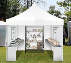 a white tent is set up in the grass with bottles and cups on shelves under it