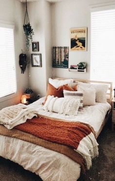 a bed with white sheets and orange blankets in a small room next to two windows