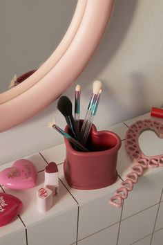 there is a pink cup with makeup brushes in it on the counter next to a mirror