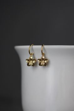 "Sweet and delicate 18k gold vermeil Plumeria flower charms dangle from 24k gold vermeil post hoops. The perfect go-to-earrings for any occasion and any age. Gold flower charms: 11x11mm Total length of earrings: almost 1\" All gold is gold vermeil, gold plating over sterling silver. A matching necklace is available... www.etsy.com/listing/1574987377/plumeria-flower-necklace As the owner, maker, designer, and curator of this shop, I take great pride in providing you with jewelry that you will lov 14k Gold Earrings With Flower Charm For Gift, Gold Flower Charm Earrings In 14k Gold, Gold Plated Flower Charm Earrings, Yellow Gold Flower Charm Earrings, Delicate Gold Huggie Earrings With Ear Wire, Delicate Gold Brass Hoop Earrings, Delicate Gold Hoop Earrings In Brass, Dainty Hoop Earrings With Flower Charm, Gold Delicate Hoop Earrings