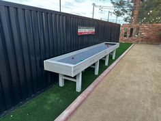 an outdoor shuffle table in front of a black wall and green artificial grass with lights strung from above