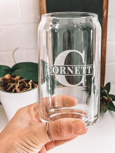 a person holding up a glass with the word gornett on it in front of a potted plant