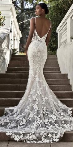 a woman is standing on some stairs wearing a wedding dress with an open back and floral appliques