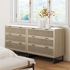 a white couch sitting in front of a window next to a dresser with two vases on top of it