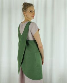 a woman standing in front of a white curtain wearing a green and pink dress with pockets